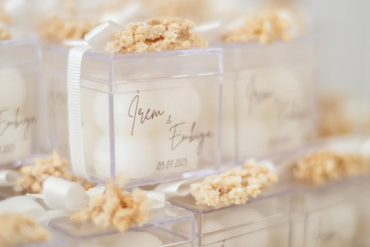 Photo by ömer aliko on Pexels Clear wedding favor boxes are stacked with white ribbons and dried flowers.