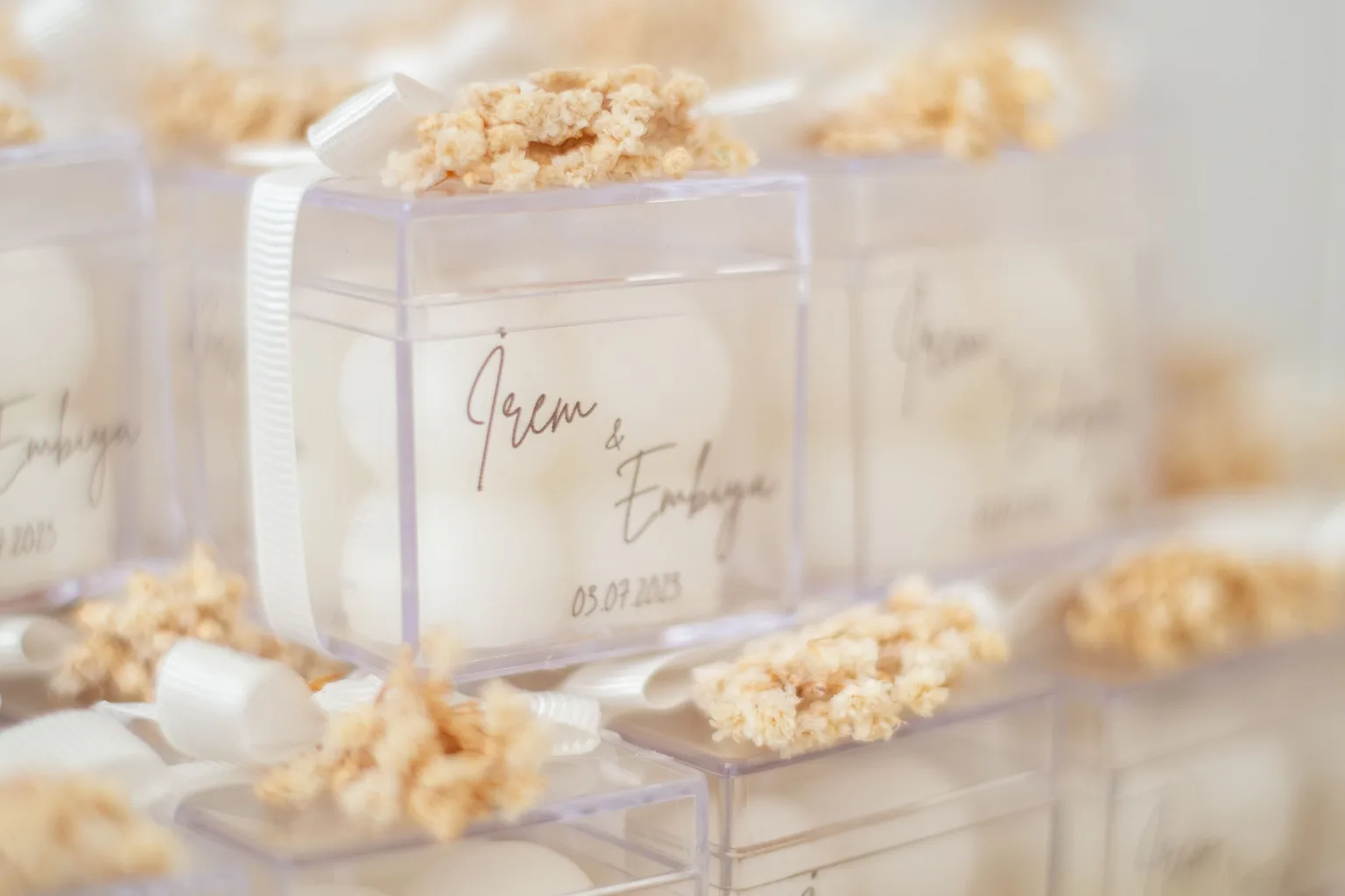 Photo by ömer aliko on Pexels Clear wedding favor boxes are stacked with white ribbons and dried flowers.