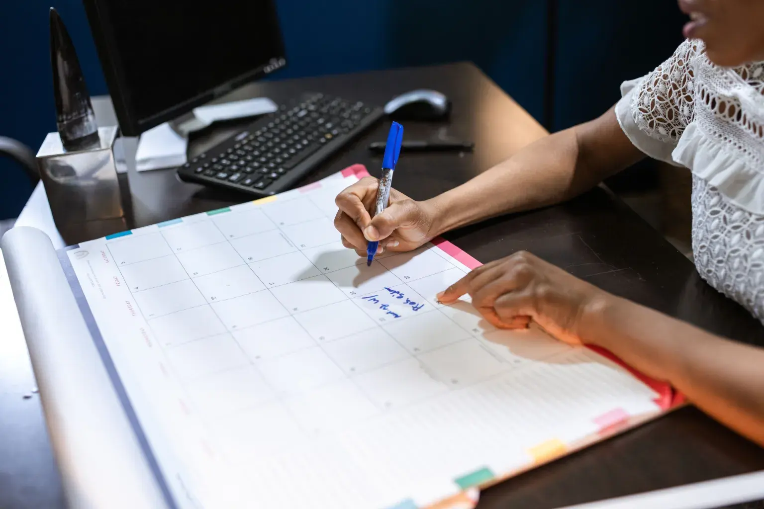 Photo by RDNE Stock project on Pexels A person writes a note on a large desk calendar with colored tabs.