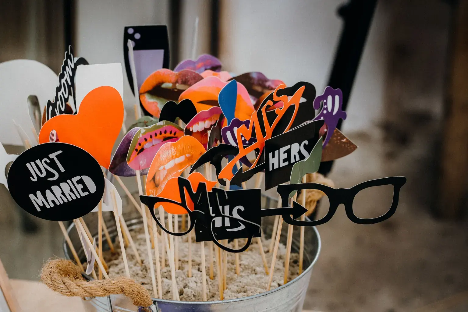 Photo by Rene Terp on Pexels Wedding photo booth props on sticks stand in a metal bucket, including a Just Married sign and glasses.