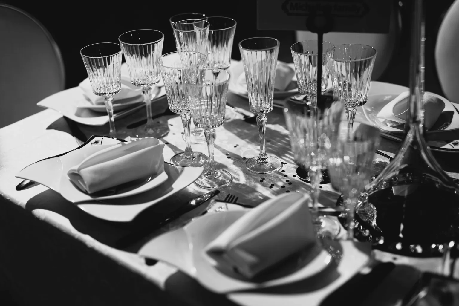 Photo by NUDE Nahum on Pexels A black-and-white reception table is set with plates, folded napkins, crystal glasses, and place settings.