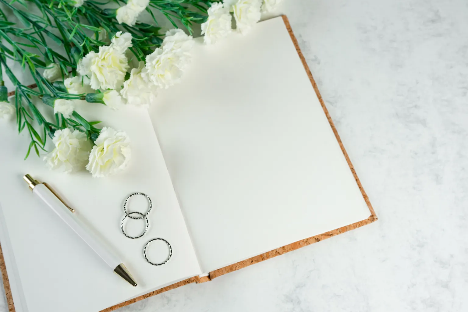 Photo by Ylanite Koppens on Pexels Three silver rings rest on a blank notebook beside a pen and white flowers.