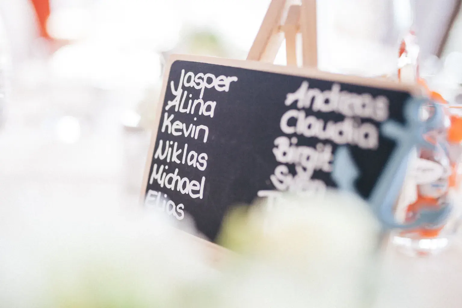 Photo by Heiner on Pexels A small chalkboard on an easel lists guest first names at a wedding reception table.