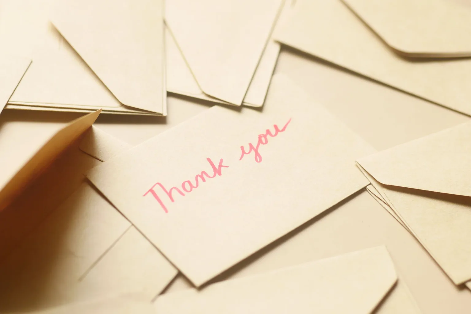 Photo by Towfiqu barbhuiya on Pexels A card with pink Thank you lettering rests among cream envelopes.