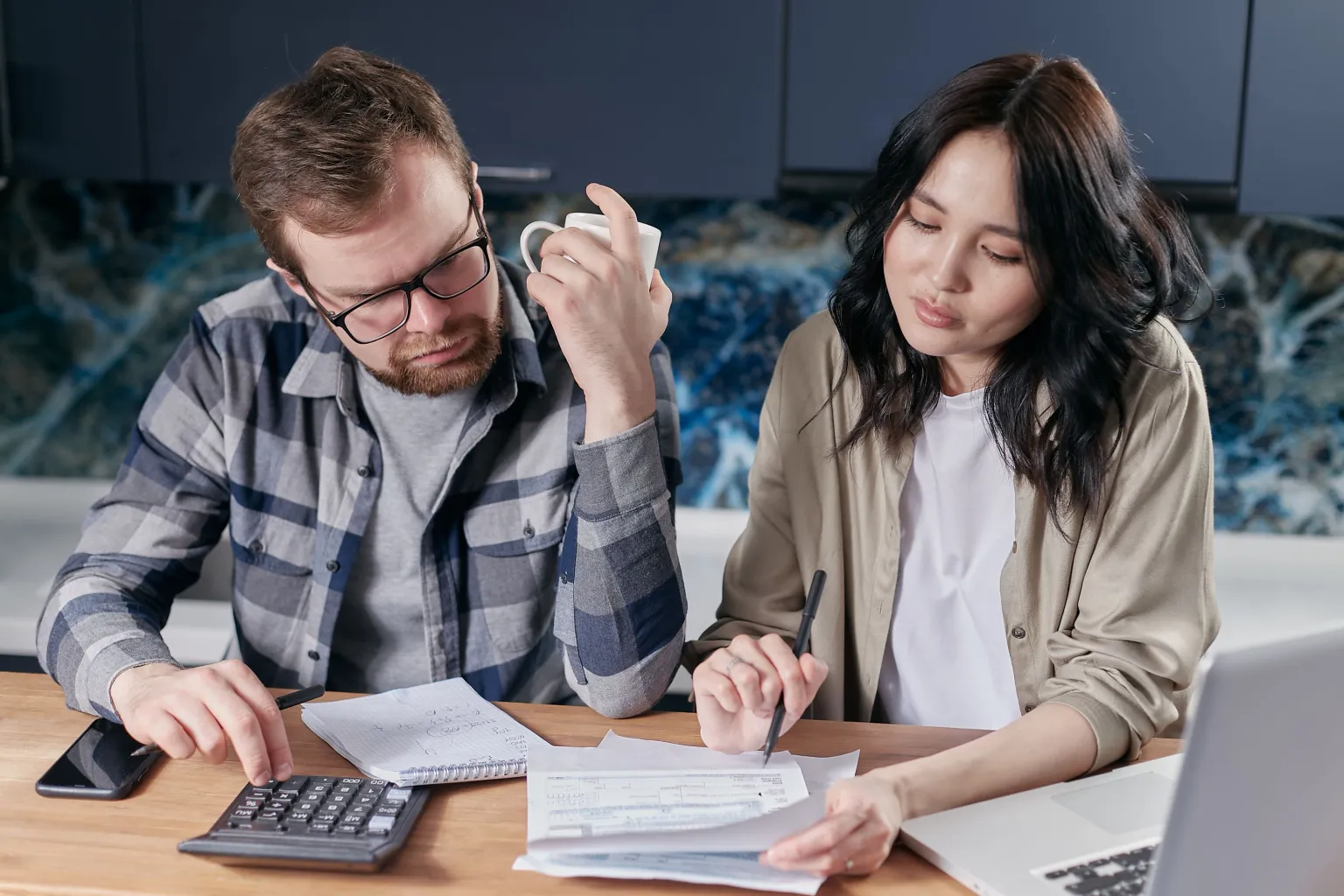 Photo by Mikhail Nilov on Pexels Two people review papers together at a kitchen table with a calculator, phone, and laptop.