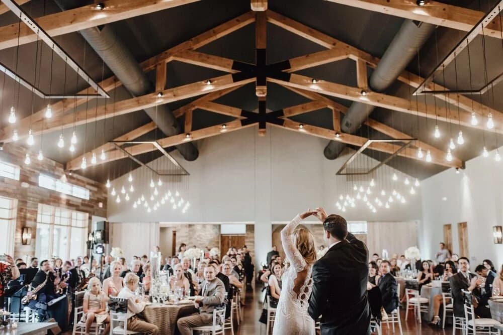 Reception Hall with wood trusses, hanging lights, dining tables, and a dance floor