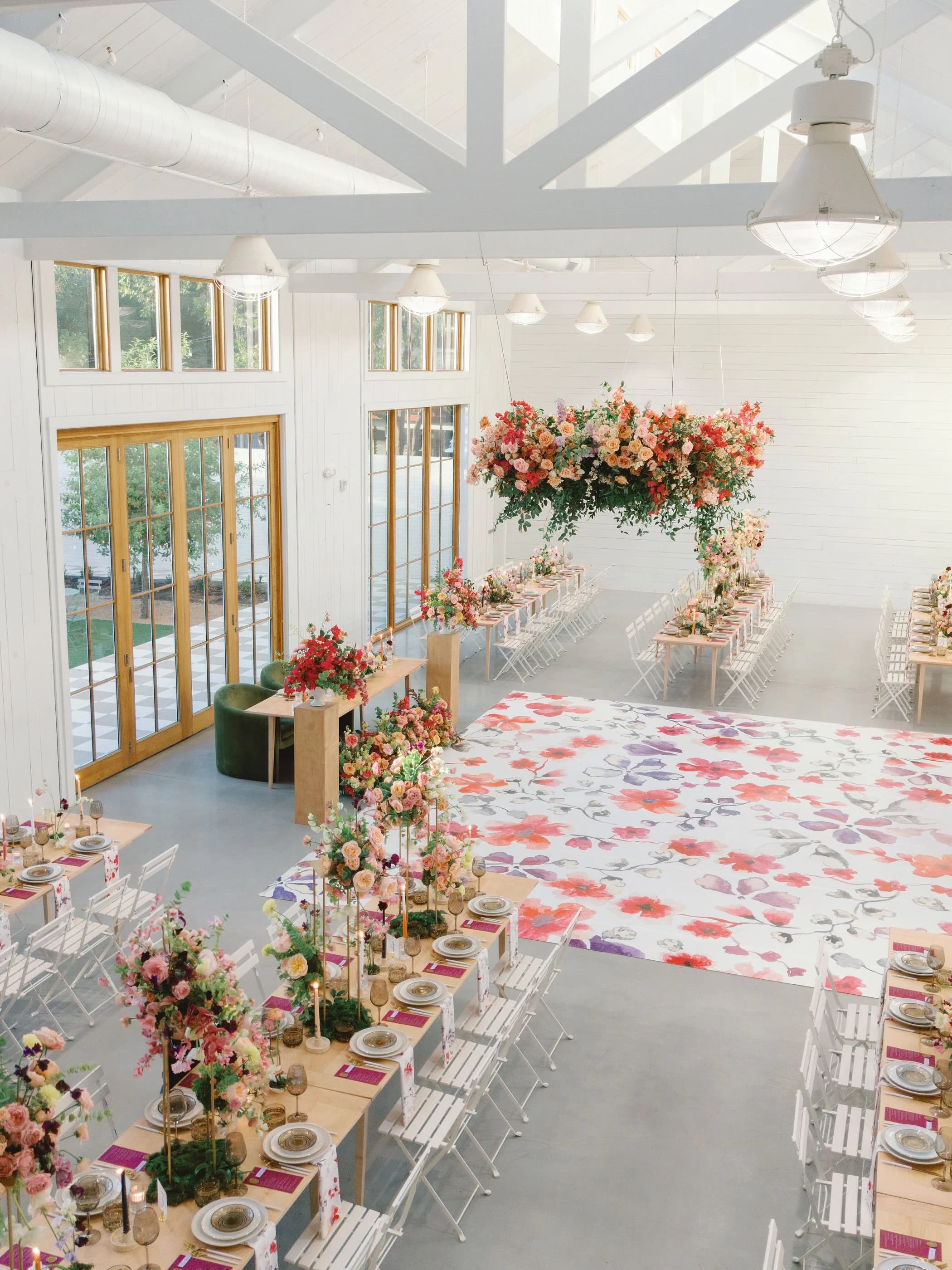 Bright reception hall with white beams, long dining tables, flowers, and a painted dance floor
