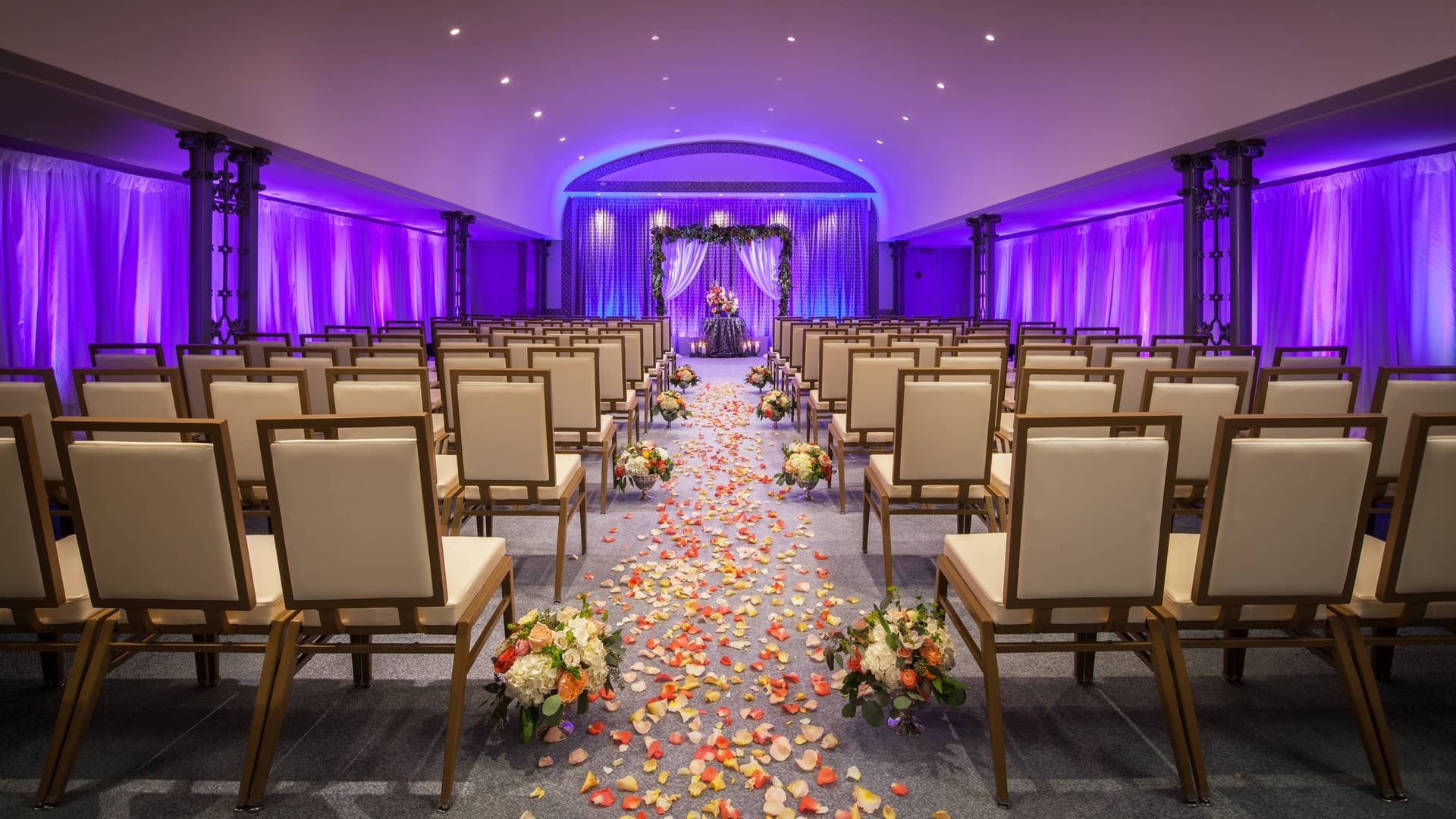 The St. Anthony ceremony room with purple lighting, floral aisle decor, and rows of chairs