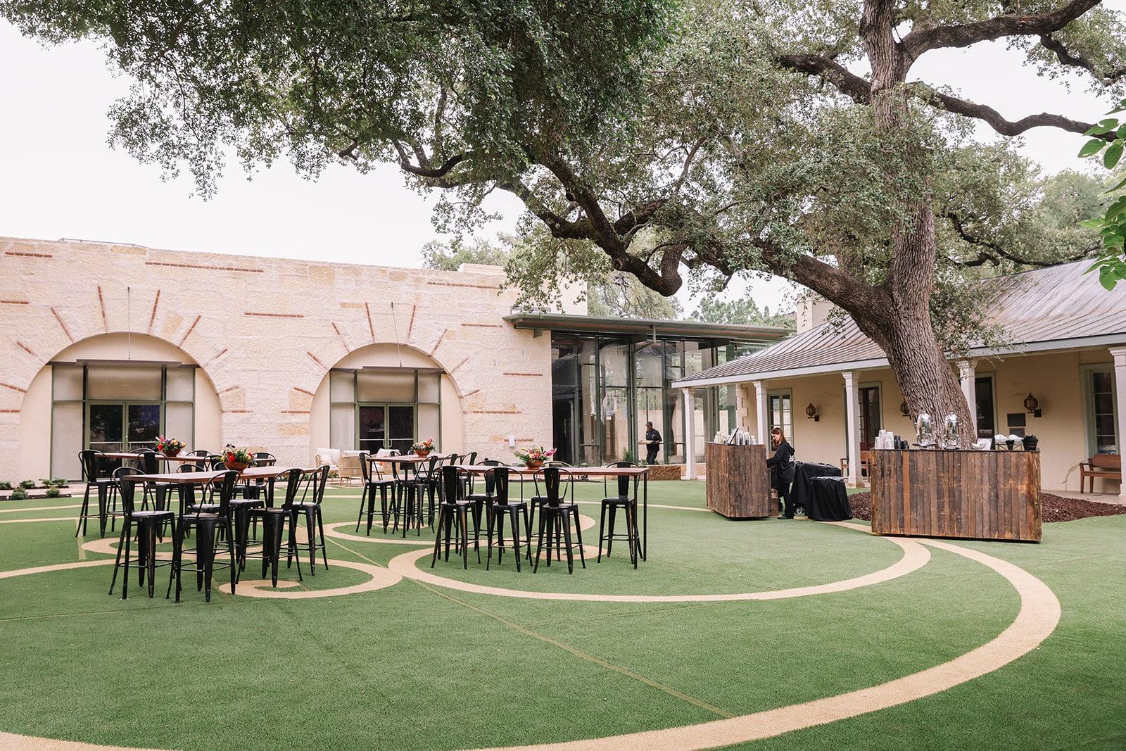 Dawson Family Hall courtyard set with cocktail tables beneath mature oak trees