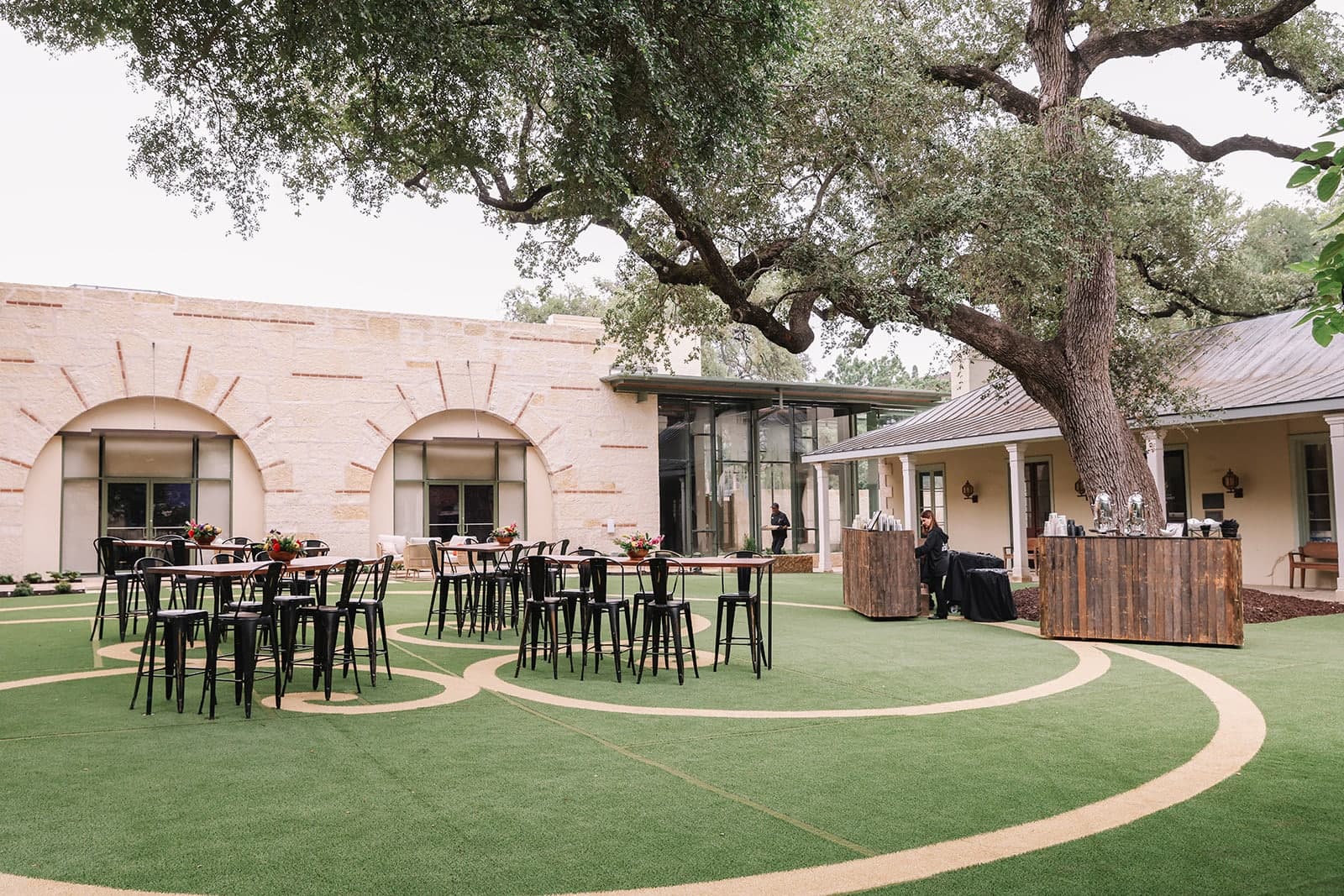 Dawson Family Hall courtyard set with cocktail tables beneath mature oak trees